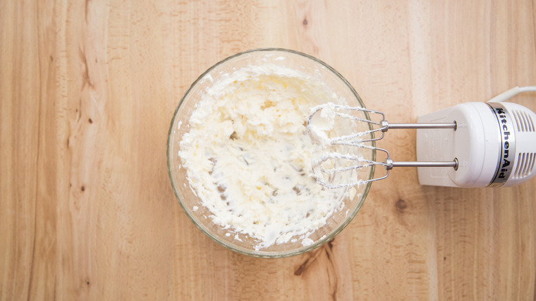 cream cheese frosting in bowl next to hand mixer