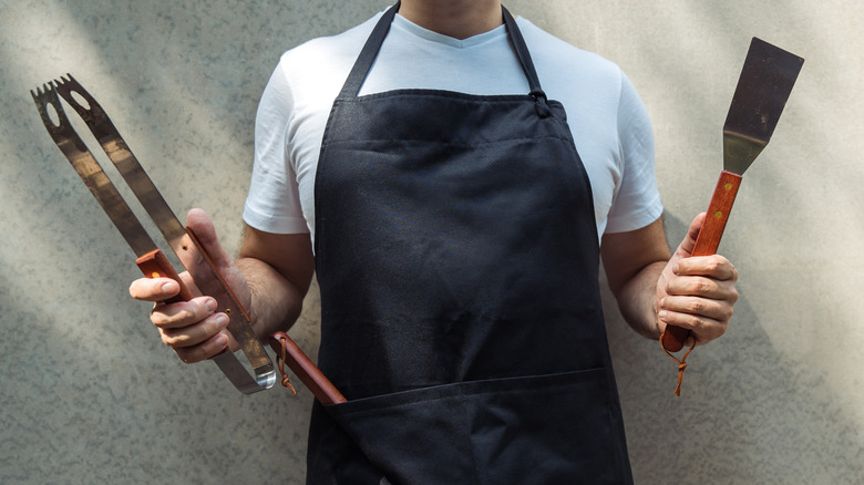 Person wearing apron holding barbecue tools