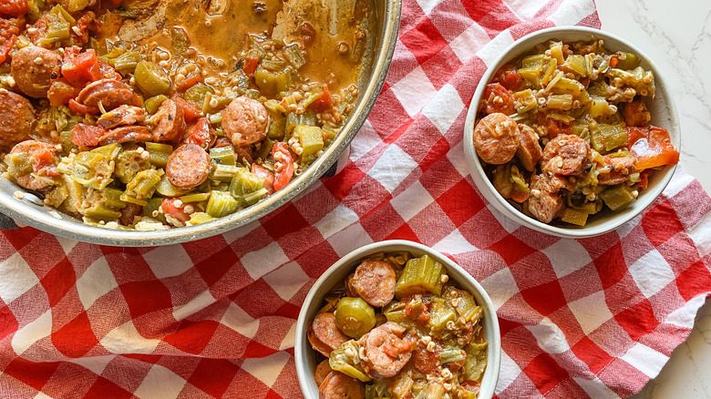 Overhead shot of a metal bowl and two smaller bowls filled with stewed okra and tomatoes with sausage