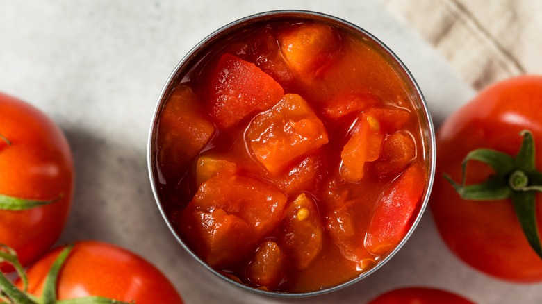 canned tomatoes surrounded by fresh tomatoes