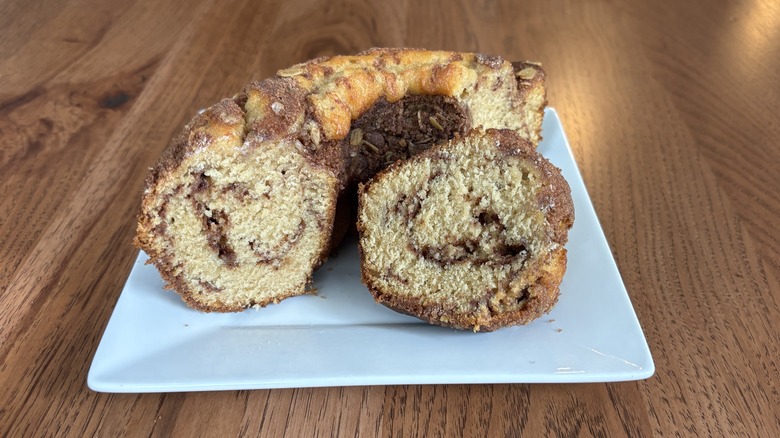 Slice of coffee cake on plate with rest of cake behind it