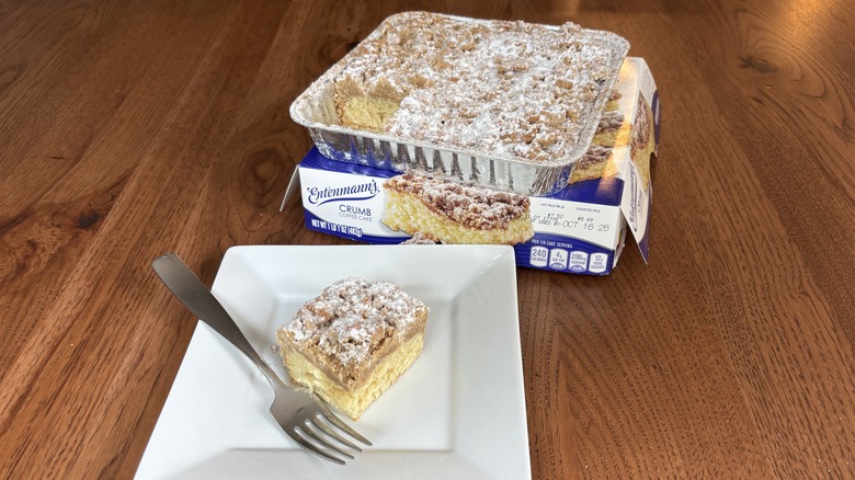 Square slice of coffee cake on plate with box and cake behind