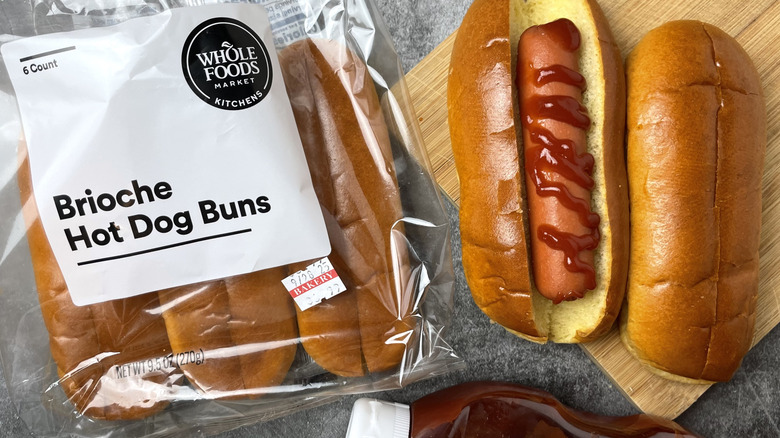 A package of Whole Foods Brioche Hot dog buns next to a hot dog with ketchup on it