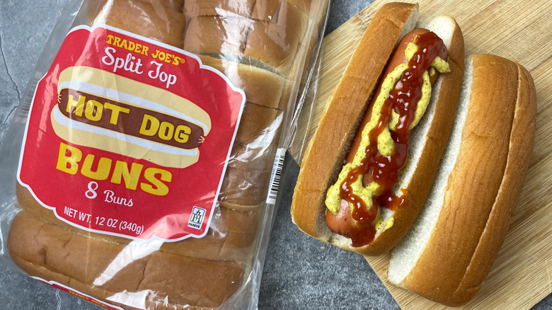 A package of Trader Joe's Split top hot dog buns next to a hot dog with ketchup and mustard on it
