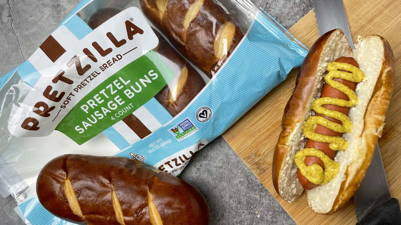A package of Pretzilla pretzel sausage buns next to a hot dog with mustard on it
