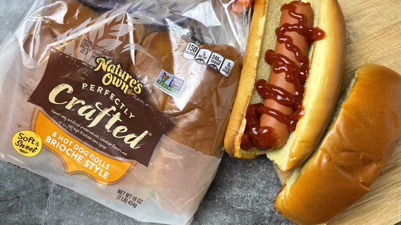 A package of Nature's Own Brioche style hot dog buns next to a hot dog with ketchup on it