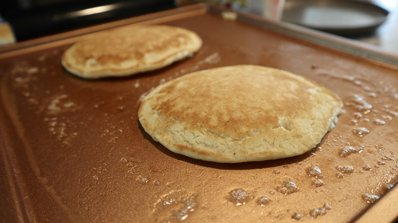 two pancakes on copper colored griddle