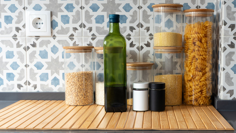 Pasta and grains in clear glass jars and a dark bottle of olive oil on a kitchen counter