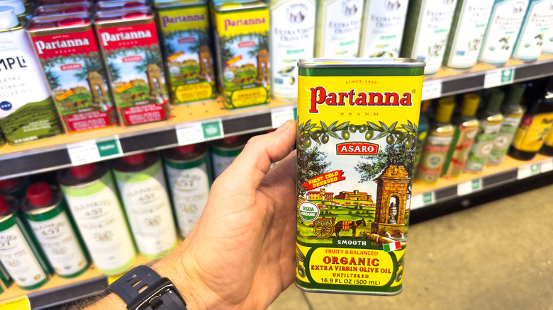 Hand holding a tin of olive oil in a grocery store in front of a shelf