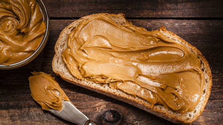 Bread with peanut butter, a knife, and jar of peanut butter