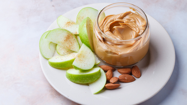 Peanut butter in a jar with apples and almonds on the side