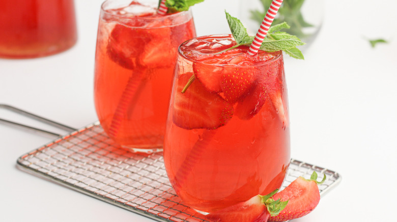 Two glasses of strawberry sweet tea with stripped straws garnished with strawberries and mint