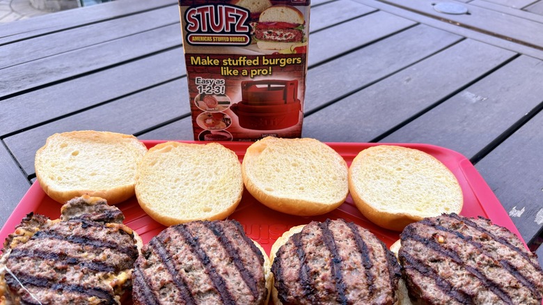 A tray of grilled stuffed burgers on buns next to the Stufz burger press by As Seen On TV