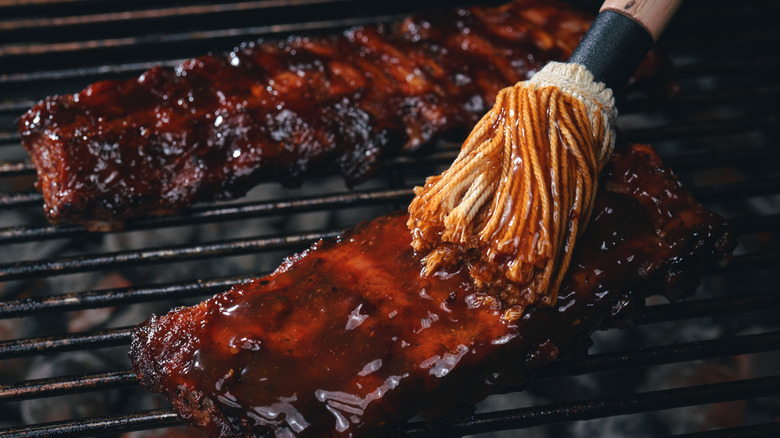 Brush applying sauce to ribs on grill.