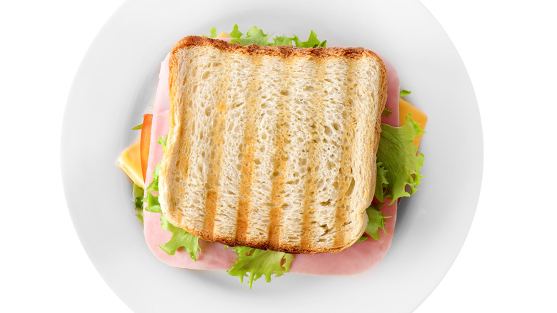An uncut, toasted ham and cheese sandwich on a white plate