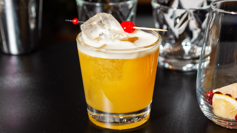 Classic whiskey sour with cherry and ice cubes