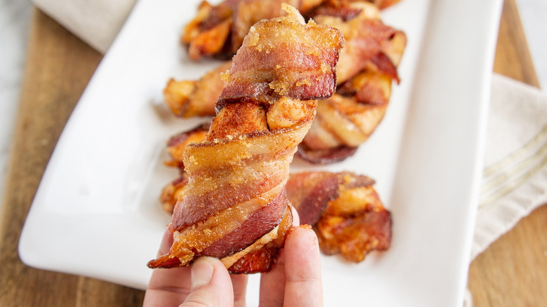 a bacon wrapped chicken tender held in a hand above a plate