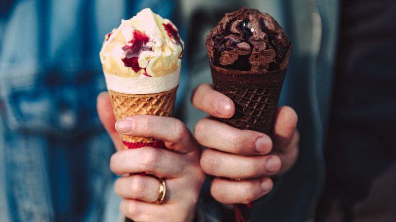 Two hands holding a vanilla and berry ice cream cone and a chocolate cone