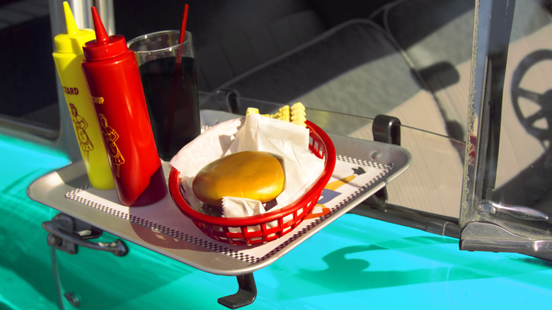 Burger and a drink on a tray attached to a car