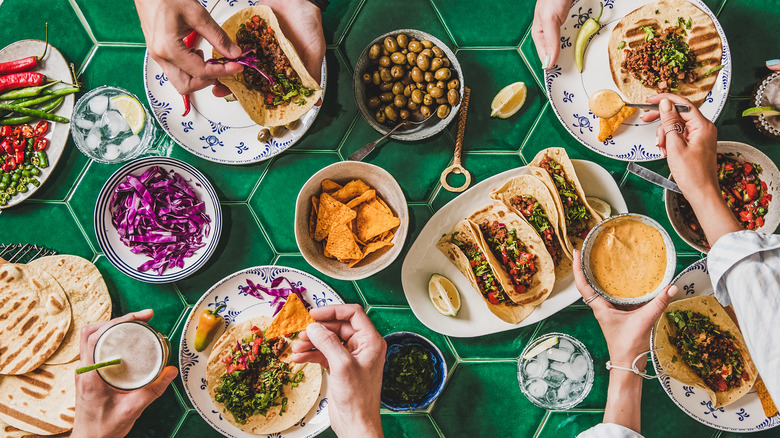 Hands fixing several plates of tacos with toppings.