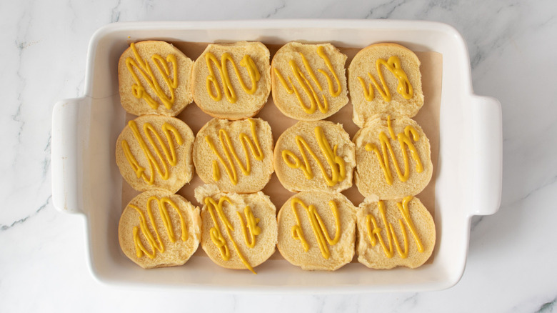 Bottom buns drizzled with mustard in baking dish