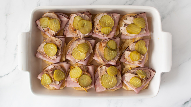 Uncapped pork sliders topped with pickles in baking dish