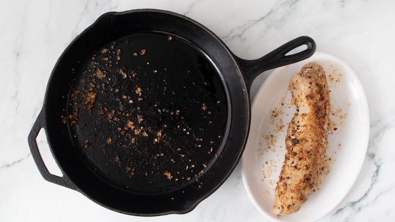 Cast iron skillet next to pork tenderloin on plate