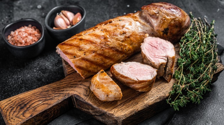 Grilled pork tenderloin on a cutting board with thyme