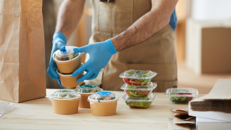 Restaurant worker wearing blue gloves putting together a takeout order