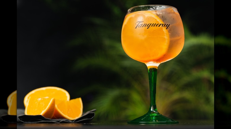 A Tanqueray glass next to orange slices.