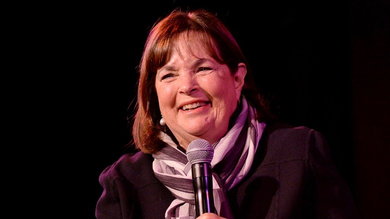 Ina Garten holding a microphone and laughing on stage at an event