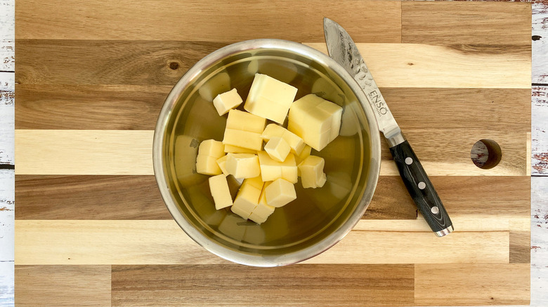 Butter cubes in bowl on cutting board with knife