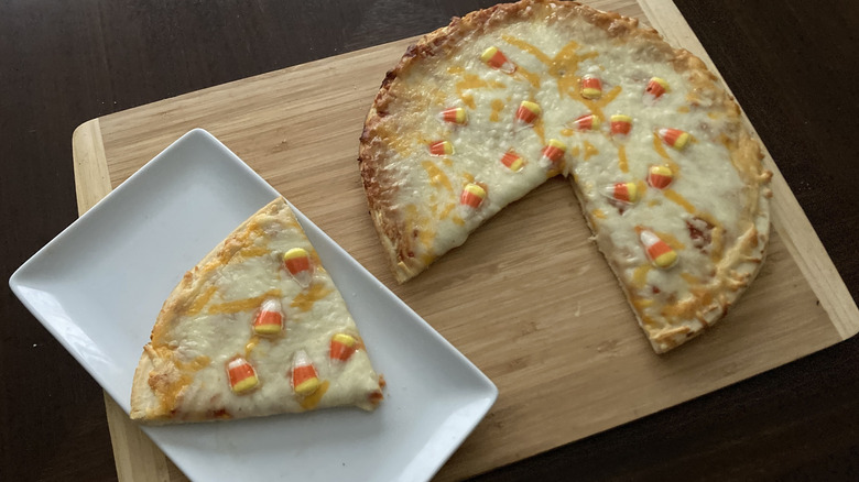 Tombstone five cheese candy corn pizza on a board with a slice on a plate
