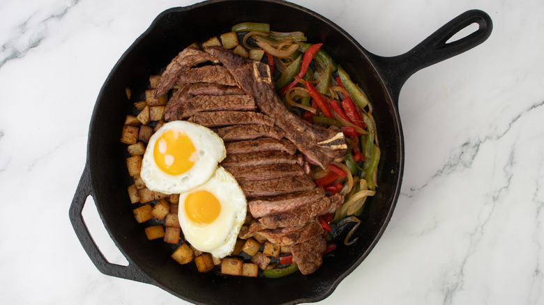 skillet with steak, potatoes, veggies, and eggs