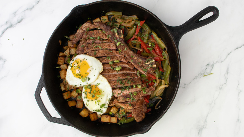 skillet with steak, potatoes, veggies, and eggs garnished with scallions and cilantro