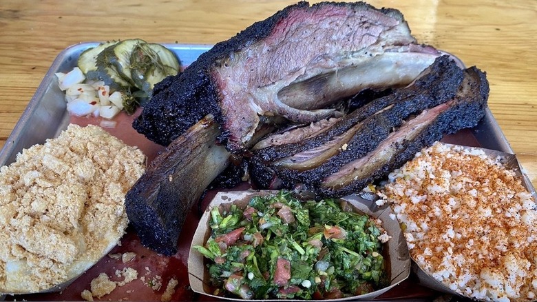 An oversized rib and sliced brisket on a tray with paper boats filled with sides.