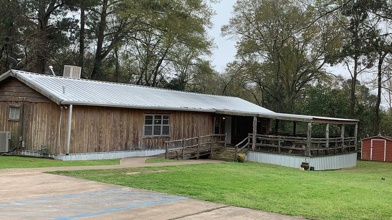 A wood paneled mobile home with a tin roof and a large deck under trees.