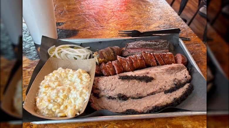 A metal tray loaded with brisket, sausage, and a side of creamed corn.