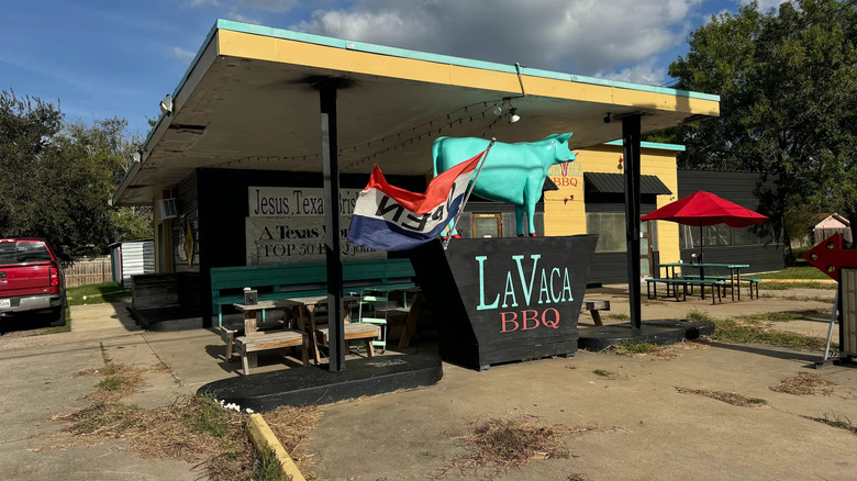 Statue of a turquoise cow placed in front of a small, yellow barbecue joint called La Vaca BBQ.