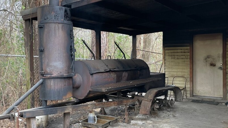 An old smoker on a wooden porch with trees in the background.
