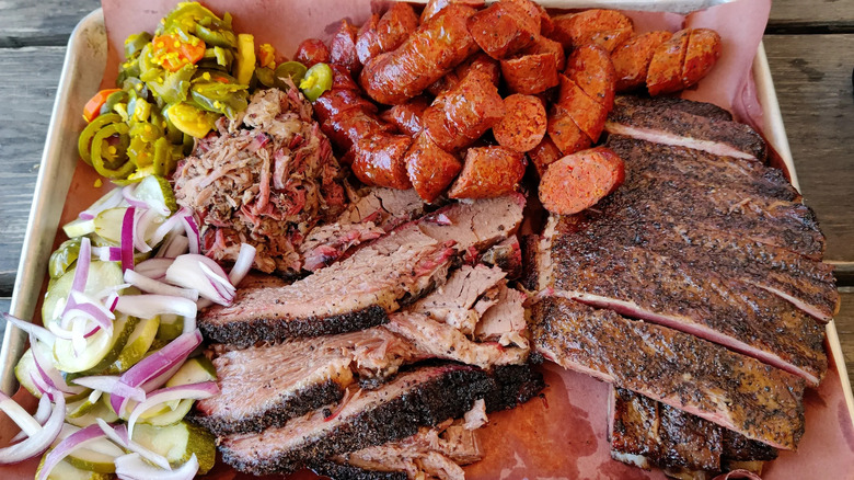 A metal tray covered with butcher paper and generous servings of sliced brisket, sausage, and ribs.