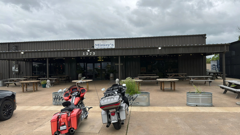Two motorcycles parked in front of gray, steel rectangular building.