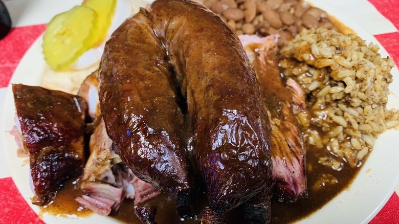 A large sausage link stacked on top of ribs next to rice and beans on a white plate.