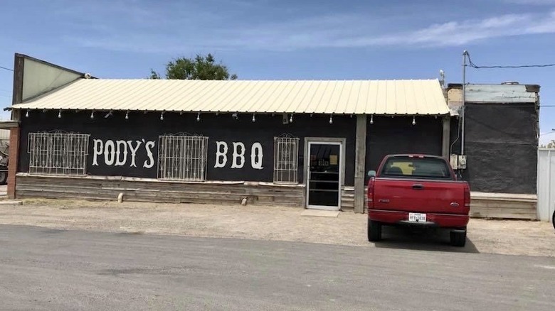 A red pick up truck parked by a western style building that says Pody's BBQ in white letters on the side.