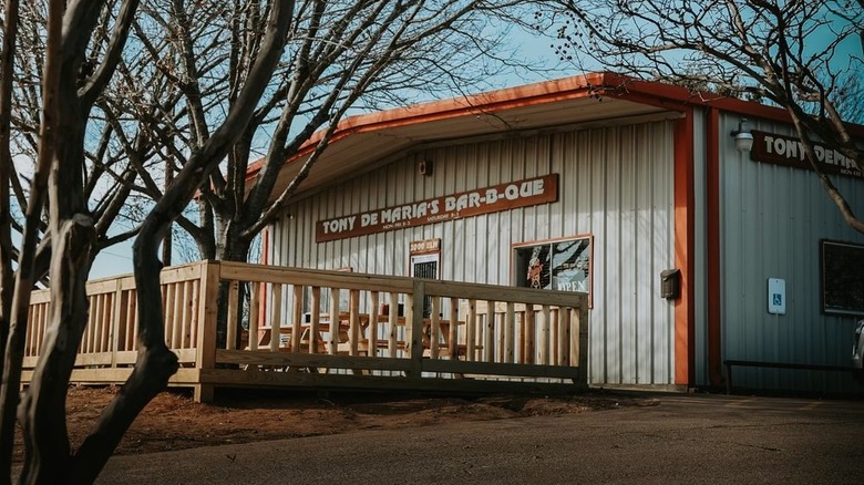 A corrugated steel building with red trim and a wooden deck with picnic tables.