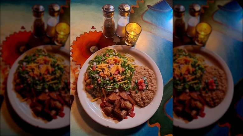 Plate with green chile-smothered pork tamales, refried beans, and fried potatoes with peppers.