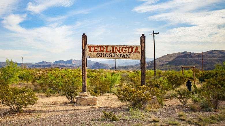 Sign reading "Terlingua Ghost town" during daytime in the middle of a desert landscape.