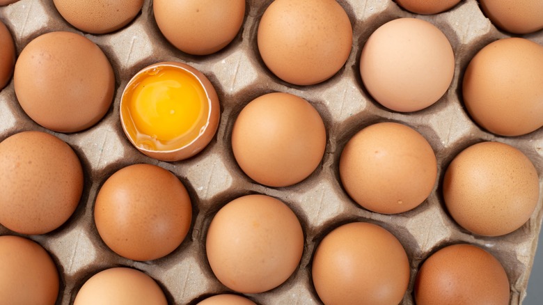 Eggs in a carton with one cracked open egg exposing the yolk