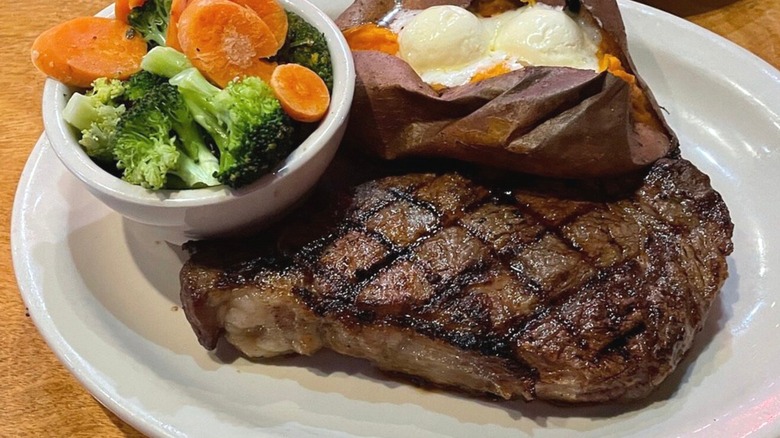 Grilled steak served with a baked sweet potato and a side of steamed carrots and broccoli