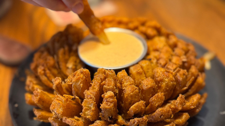 Hand dipping an onion from Outback Steakhouse's Bloomin' Onion into sauce